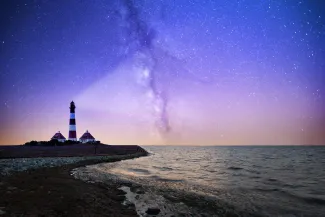 white and red lighthouse near bodies of water at night by Robert Wiedemann courtesy of Unsplash.